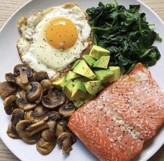 a white plate topped with salmon, mushrooms and an egg on top of it next to spinach