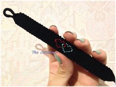 a hand holding a black crochet bracelet with a red heart on it