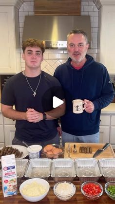 two men standing next to each other in front of a counter with food on it