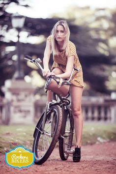 a woman riding on the back of a bike down a dirt road with trees in the background