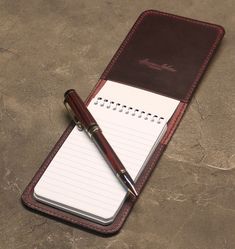 a notepad with a pen on top of it next to a brown leather case