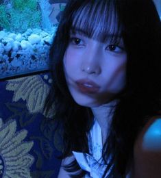 a woman sitting in front of an aquarium looking at the camera with blue light on her face