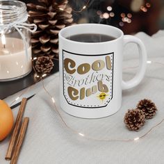 a coffee mug sitting on top of a table next to some pine cones and candles