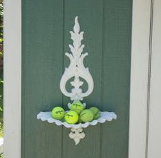 tennis balls in a bowl on the side of a green door with white trim around it