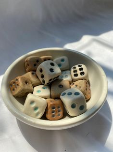 a white bowl filled with lots of dices on top of a table next to a white cloth