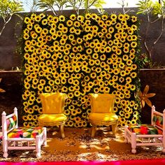 two yellow chairs sitting next to each other in front of a sunflower covered wall