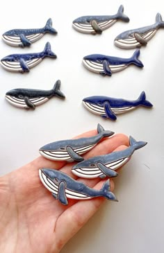 a hand holding a bunch of blue whale magnets on top of a white table