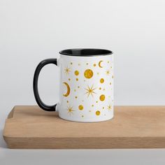 a black and white coffee mug with gold stars and moon designs on it sitting on a wooden surface