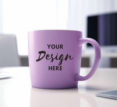 a purple coffee mug sitting on top of a white table next to a laptop computer