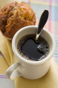 a cup of coffee next to a muffin on a napkin with a spoon in it