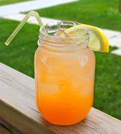 a mason jar filled with orange liquid and lemon wedges on a wooden table outside