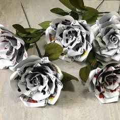 four white roses with black and red designs are on the floor next to some green leaves