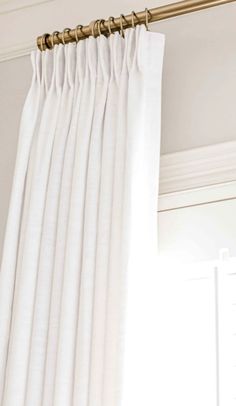 a white curtain hanging from the side of a window with gold hardware on it's rod