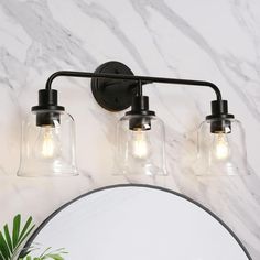 a bathroom vanity light with two clear glass jars on the wall and a round mirror