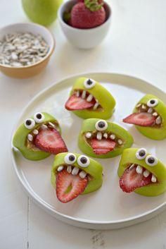 some green apples with strawberries in the shape of monster faces and eyes on them