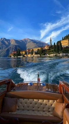 the back end of a boat traveling down a lake with mountains in the background and houses on the shore