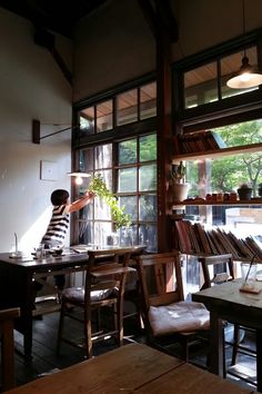 a woman standing in front of a window next to a table with books on it