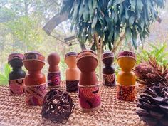 an assortment of wooden dolls sitting on top of a table next to pine cones and plants