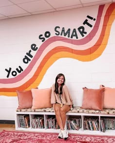 a woman is sitting on a bench in front of a wall with bookshelves