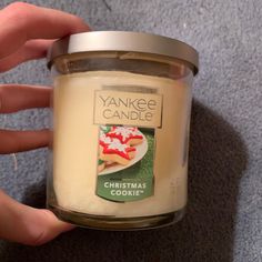 a person holding a jar of yankee candle on the floor in front of a carpet