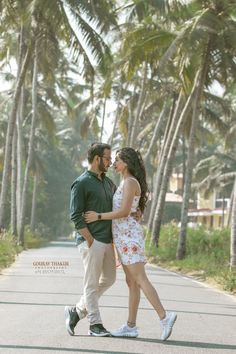 a man and woman walking down the street in front of palm trees with their arms around each other