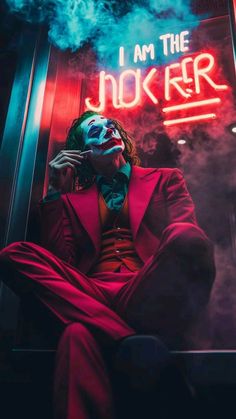 the joker is sitting in front of a neon sign