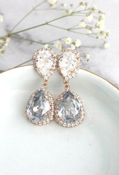 two pear shaped diamond earrings on a white plate with flowers in the backgroud