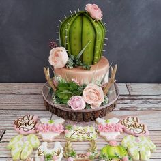 a desert themed cake and cookies on a wooden table with cactus decorations, flowers and succulents