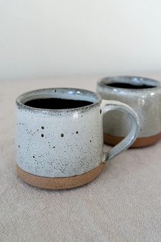 two coffee mugs sitting next to each other on top of a white table cloth