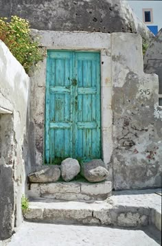 an old blue door is on the side of a stone building with steps leading up to it