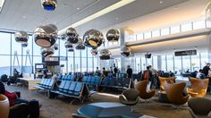 an airport filled with lots of people sitting and standing next to each other near large windows