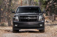 the front end of a black chevy suburban truck parked on a dirt road with trees in the background