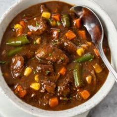 a white bowl filled with beef and vegetable stew on top of a marble countertop