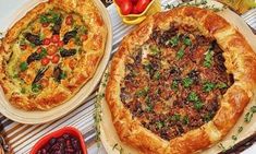 two large pizzas sitting on top of a table next to bowls of fruit and vegetables