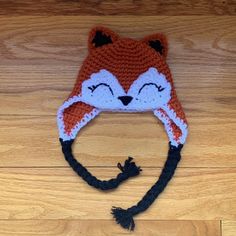 a crocheted hat with a fox design on the front and side, sitting on top of a wooden floor