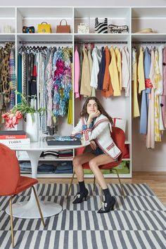 a woman sitting at a desk in front of a closet full of clothes