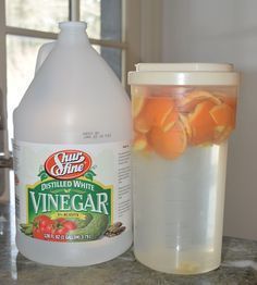 a bottle of vinegar sitting on top of a counter next to a container of oranges