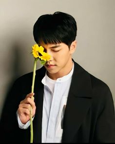 a young man holding a yellow flower in his right hand and looking down at it