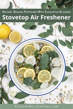 a bowl filled with lemons and leaves on top of a white table next to flowers