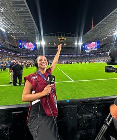 a woman is standing in front of a camera at a soccer stadium with her hand up