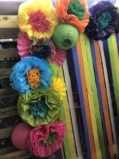 colorful paper flowers are hanging on the side of a fence