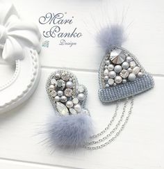 two heart shaped brooches with pearls and fur balls on white wooden surface next to decorative object