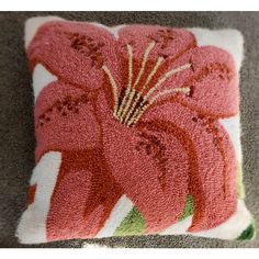 a pink flower on a white pillow with green and red trimmings sitting on the floor