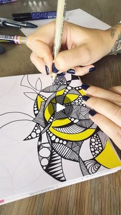 a woman's hands holding a pencil and drawing on paper with colored markers in front of her