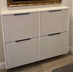 a white cabinet with two drawers and a painting on the wall in front of it