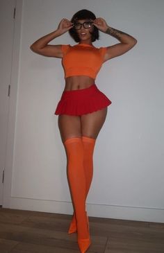 a woman in an orange top and red skirt posing for the camera with her hands on her head