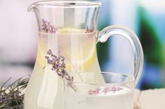 a pitcher filled with water next to a glass cup full of lemonade and lavender