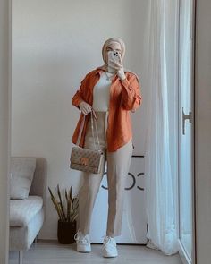 a mannequin dressed in an orange jacket and white shirt holding a purse while standing next to a couch