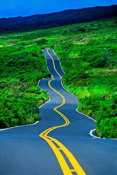 a yellow car driving down a winding road in the middle of green hills and trees