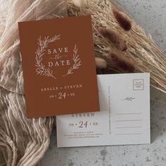 save the date cards and envelopes on top of some dried grass, next to a piece of cloth